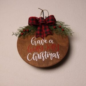 10 inch wooden circular sign with a dark oak stain. Fun font and Christmas message in white and red lettering. Complete with a checkered black and red festive bow tied around some pine and holly berry.