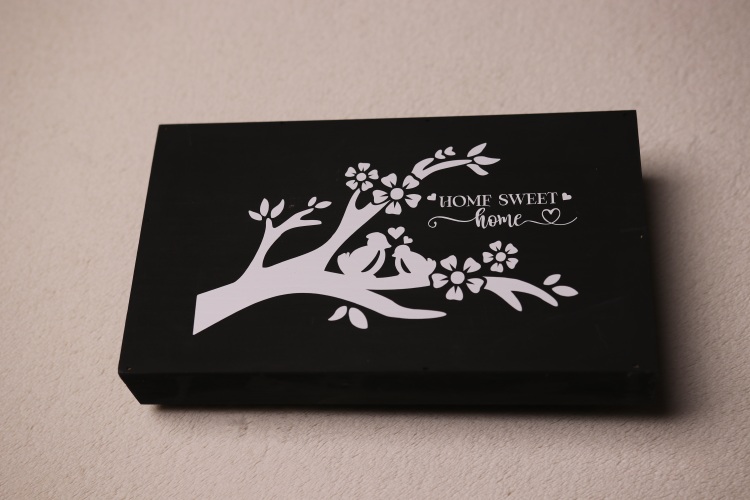 Box sign made of wood and black paint. Sign features a white painted tree branch with love birds amongst the flowers and the message "Home sweet home."