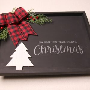 Framed wall sign for Christmas decorating. Black paint with white and silver lettering. Features a wood cutout of a pine tree with pine, holly berry and a checkered red and black ribbon for splashes of color.
