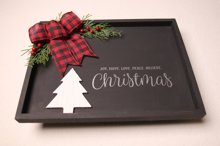 Framed wall sign for Christmas decorating. Black paint with white and silver lettering. Features a wood cutout of a pine tree with pine, holly berry and a checkered red and black ribbon for splashes of color.
