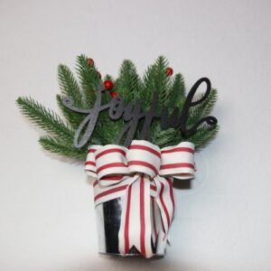 Small table-top holiday decoration. Metal pale full of faux pine needles and holly berries. Complete with wooden lettering cutout with the message "joyful" above a festive red and white Christmas ribbon.