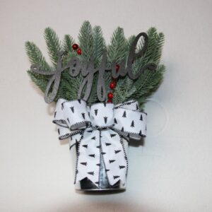 Small table-top holiday decoration. Metal pale full of faux pine needles and holly berries. Complete with wooden lettering cutout with the message "joyful" above a festive white and black Christmas ribbon featuring little pine trees.