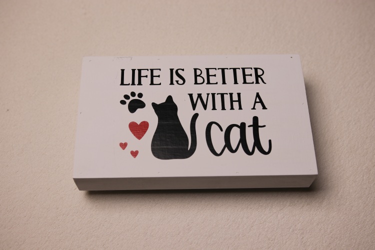 Rectangular box sign featuring a cat, paw print, and red hearts for a splash of color. "Life is better with a cat."