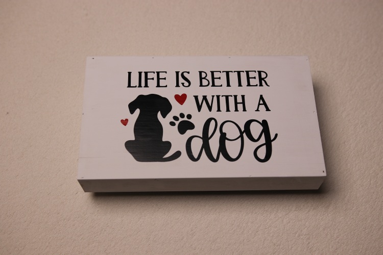 Rectangular box sign featuring a dog, paw print, and red hearts for a splash of color. "Life is better with a dog."