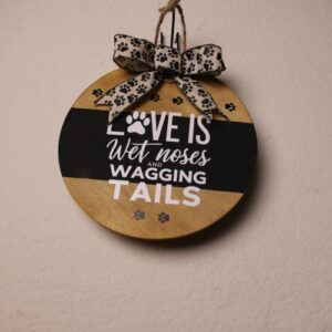 10 inch wooden circular sign with a light oak stain and a black painted stripe under white lettering. A paw print in the font and a message about the love of an animal. Fun little paw prints on the wood stain as well as a black and tan ribbon with more paw prints.