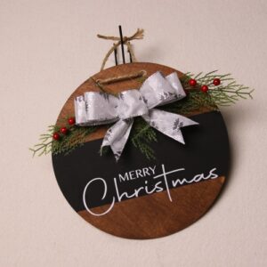 10 inch circular wooden sign with dark walnut stain and black painted strip. While lettering featuring "Merry Christmas" in a fun and festive font. Adorned with pine and holly berries tied with a white bow showing off silver pine trees.