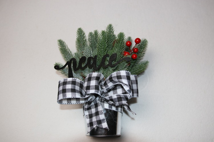 Small table-top holiday decoration. Metal pale full of faux pine needles and holly berries. Complete with cute black and white ribbon below fun, festive wood lettering reading "peace."
