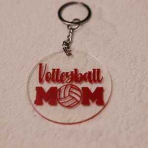 Key chain for the ultimate Volleyball Mom. Clear circular disc keychain with fun "Volleyball Mom" text. Features volleyball graphic. Red lettering and graphics.