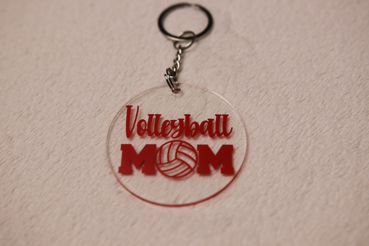 Key chain for the ultimate Volleyball Mom. Clear circular disc keychain with fun "Volleyball Mom" text. Features volleyball graphic. Red lettering and graphics.