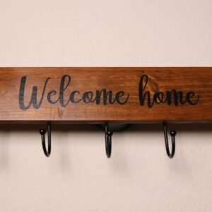"Welcome home" coat hanging sign in dark oak stain. Five coat hanging hooks in black metal.