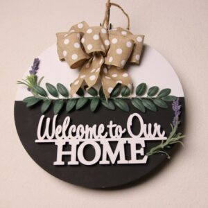 14 inch wooden circular sign with "Welcome to Our HOME" as a greeting. White and black paint with unique wood lettering cutout. A touch of small green leaves and lavendar with a brown and white polka dot bow.
