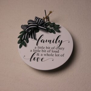 10 inch wooden circular sign painted white with whimsical black lettering. Small green leaves tied together with a black and white striped ribbon and a rustic twine hanging cord.