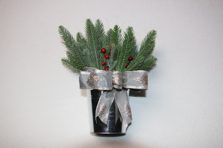 Small table-top holiday decoration. Metal pale full of faux pine needles and holly berries. Complete with holiday festive silver bow featuring glittering pine trees.